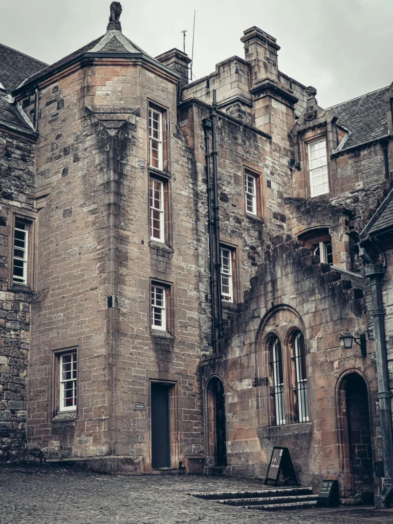 The stone front of Stirling Castle, Scotland, with mullioned windows and a cobbled courtyard under an overcast sky.
