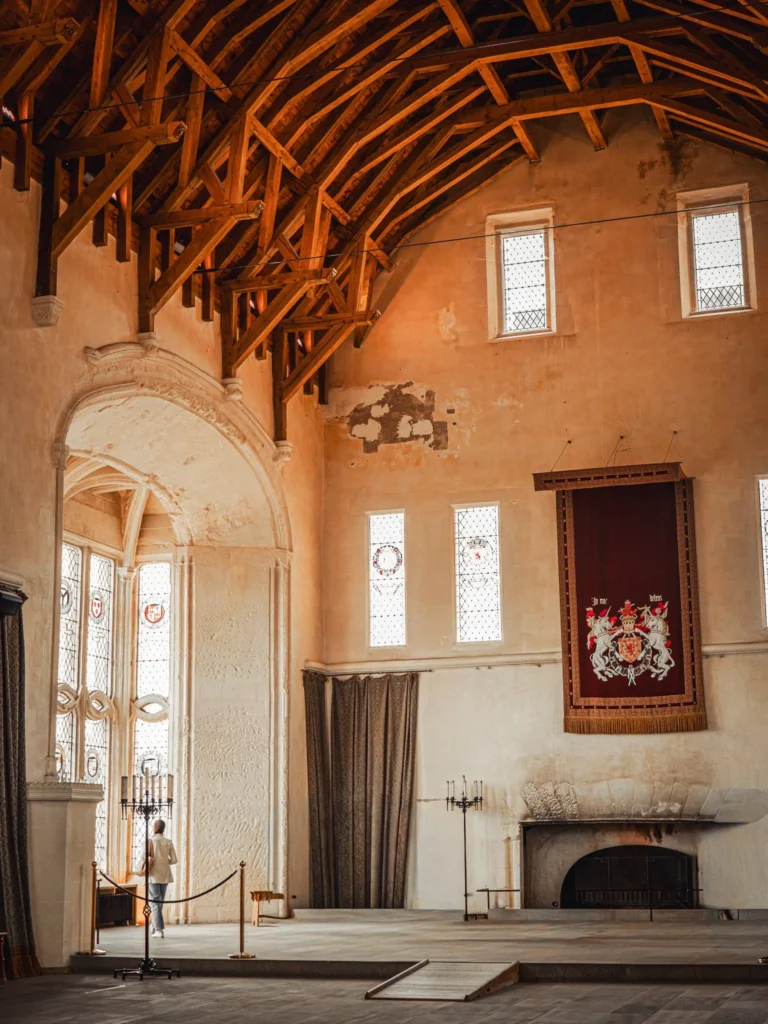 The Great Hall of Stirling Castle, Scotland, with its carved timber roof, tall windows and heraldic hangings. A visitor stands by the windows.