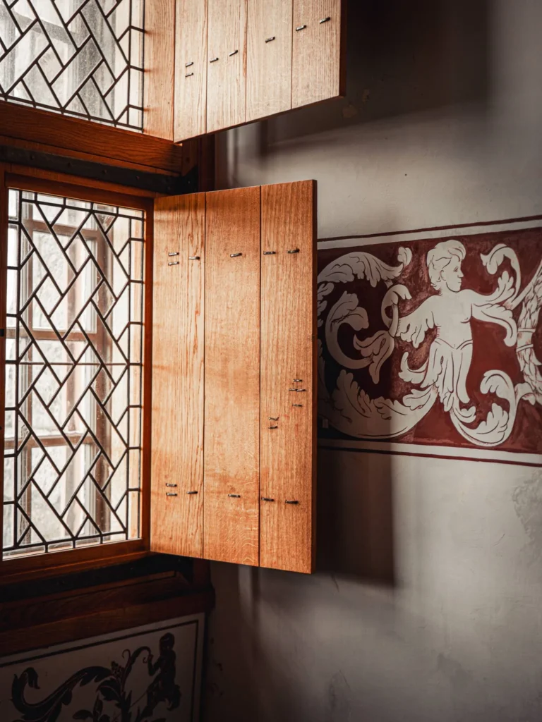 An open wooden shutter on a leaded window, with painted mural decoration on the wall inside Stirling Castle, Scotland.