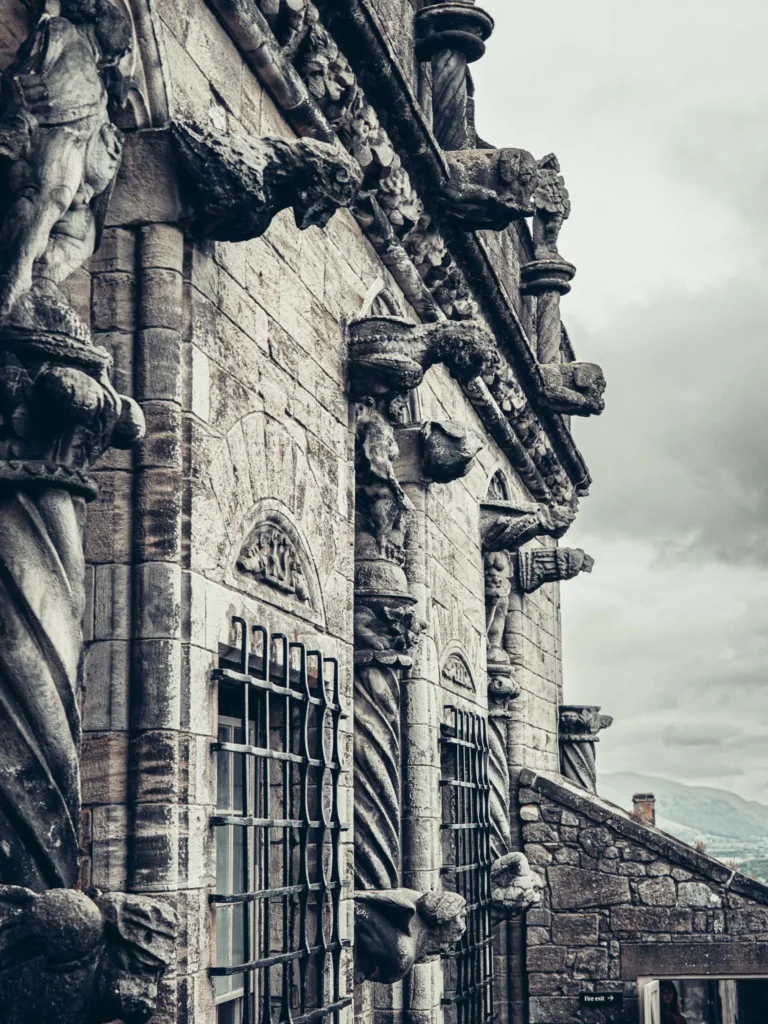 The stone front of Stirling Castle, Scotland, carved with figures and gargoyles under a cloudy sky.