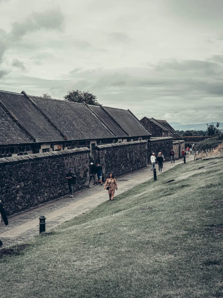 A cobbled path running along a stone wall at Stirling Castle under a cloudy sky, with a few visitors scattered along it.