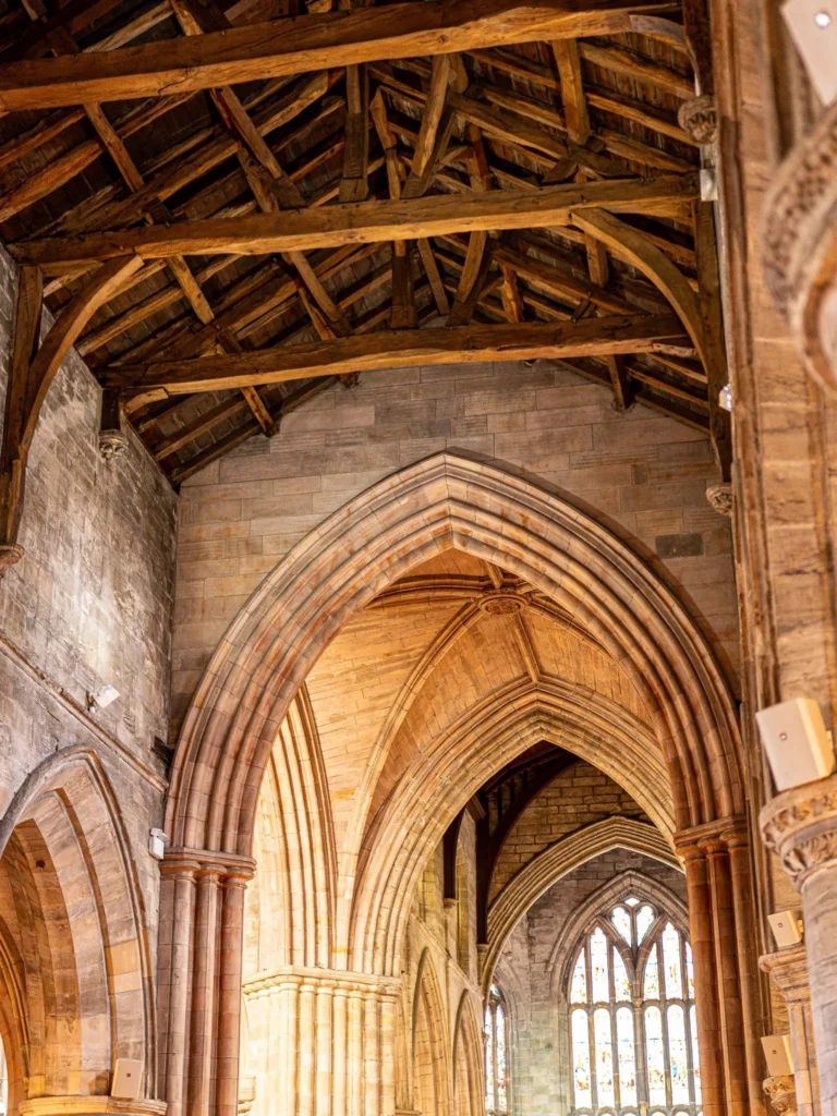 Open timber roof and stone arches of the Church of the Holy Rude in Stirling, with stained glass in the background: the exposed beam ceiling is the most striking feature inside.