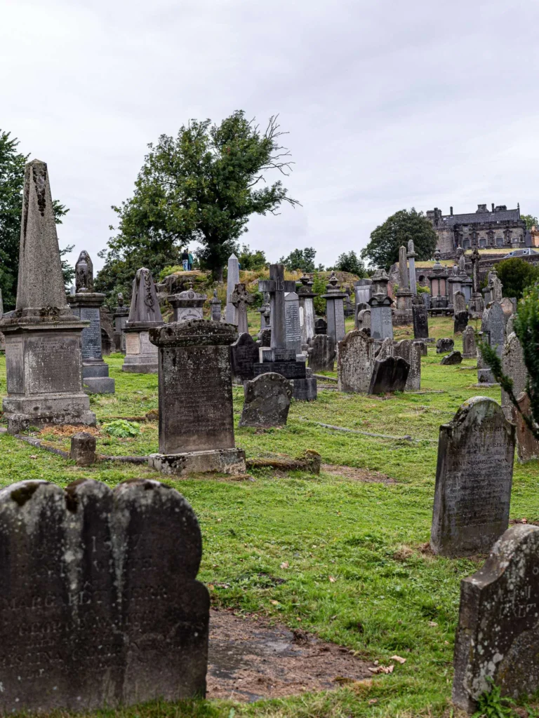 Kirkyard of the Church of the Holy Rude in Stirling, tall grass among the ancient headstones, with a panorama of the city and the bench located at the very back.