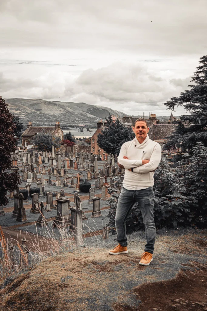 Xavier in front of the kirkyard of the Church of the Holy Rude, in Stirling, among the ancient headstones and the vegetation.