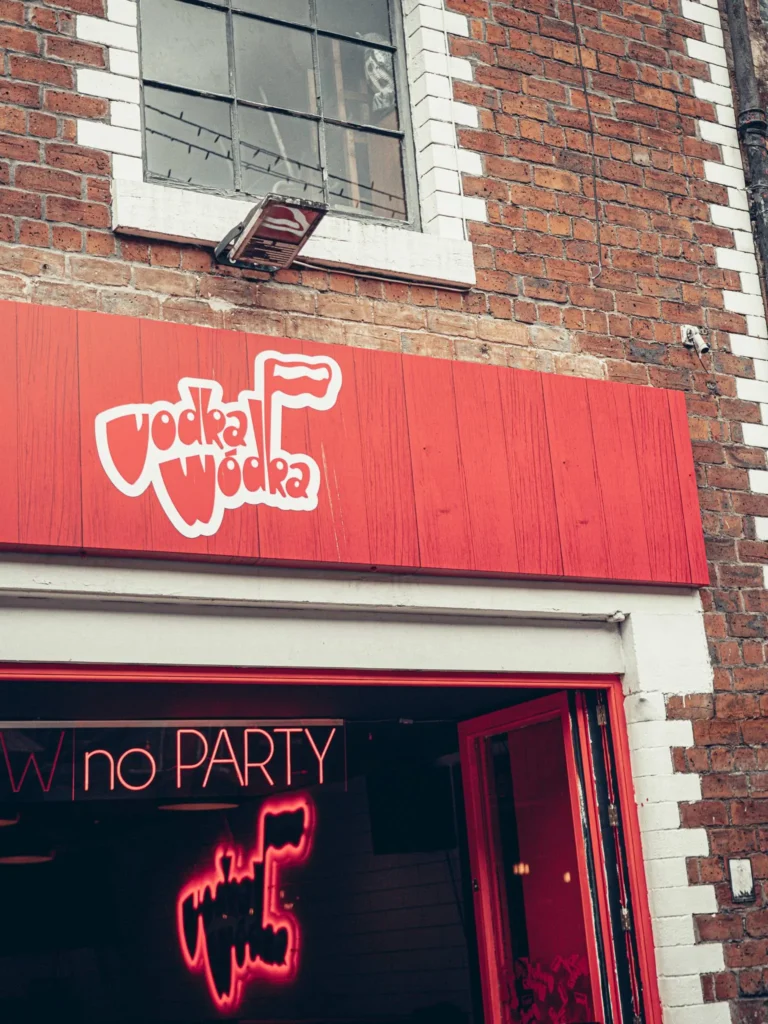 Brick facade of the Vodka Wodka bar, in the West End of Glasgow, red sign and neon visible from the inside.