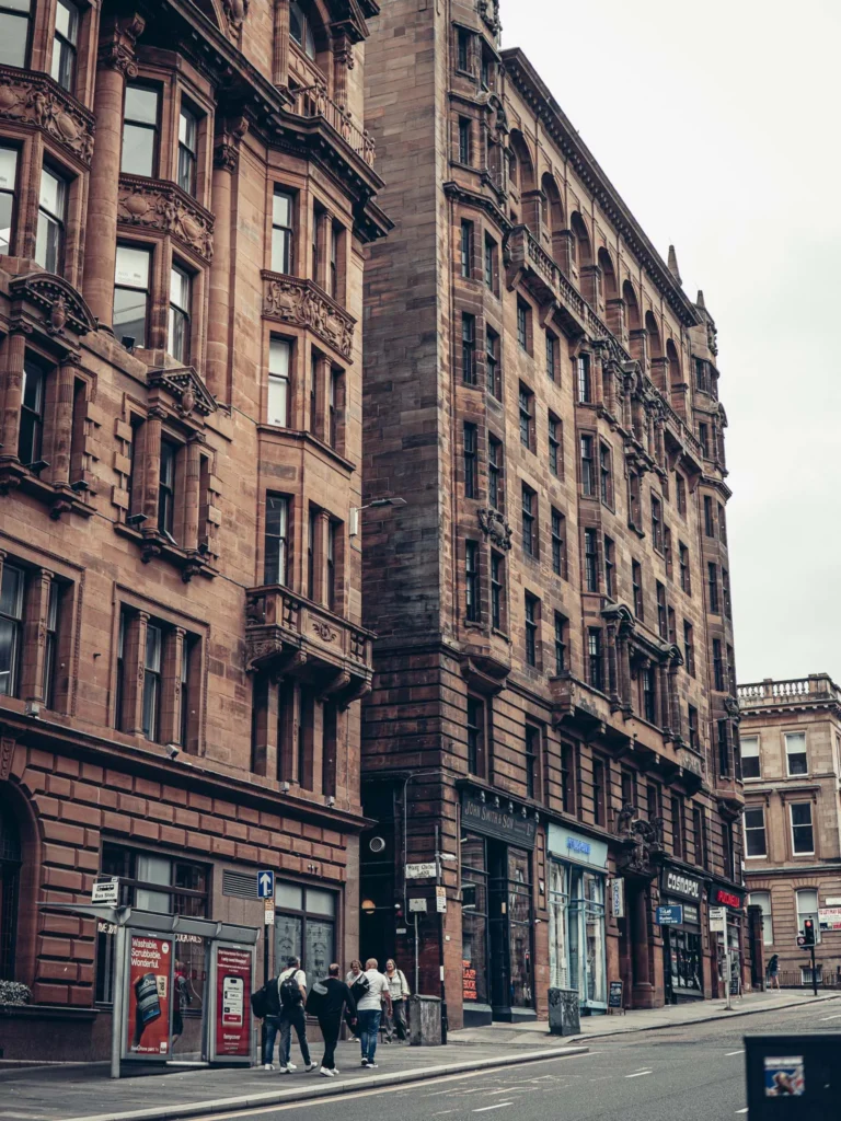 Victorian buildings in blond and red sandstone with large bay windows, a street scene in Glasgow under a changing sky.