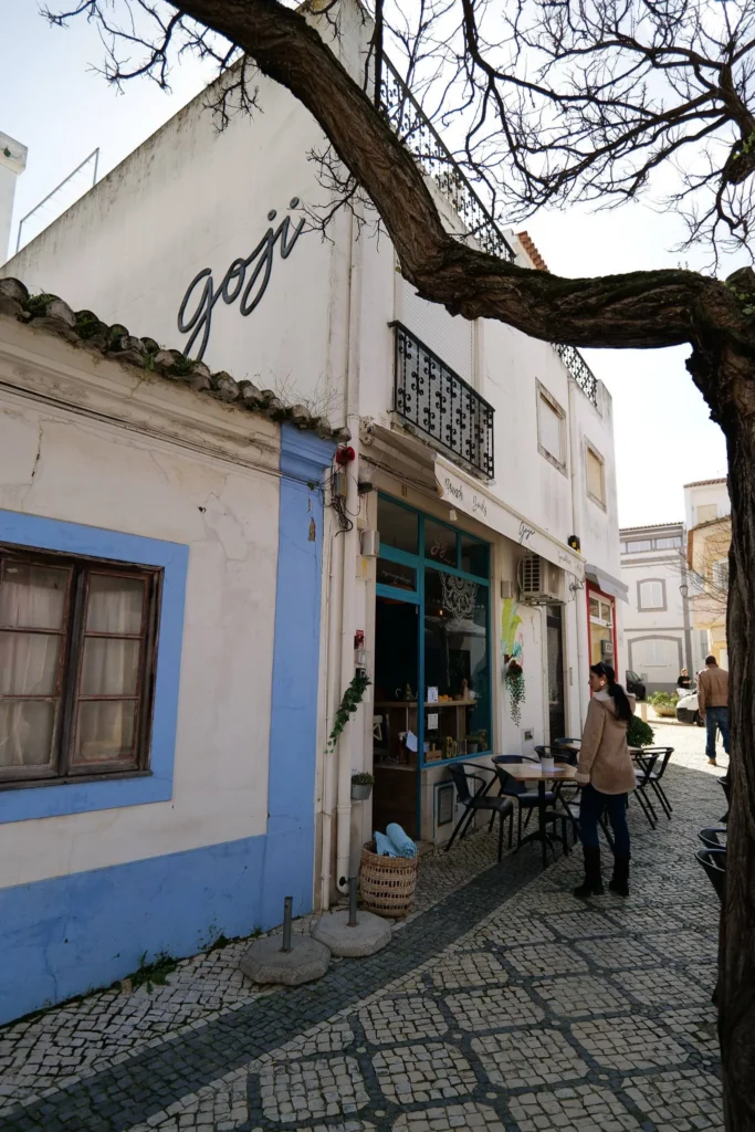 Facade of the Goji restaurant in Lagos, Algarve, with an outdoor terrace on a cobbled alley, under a leafless tree.