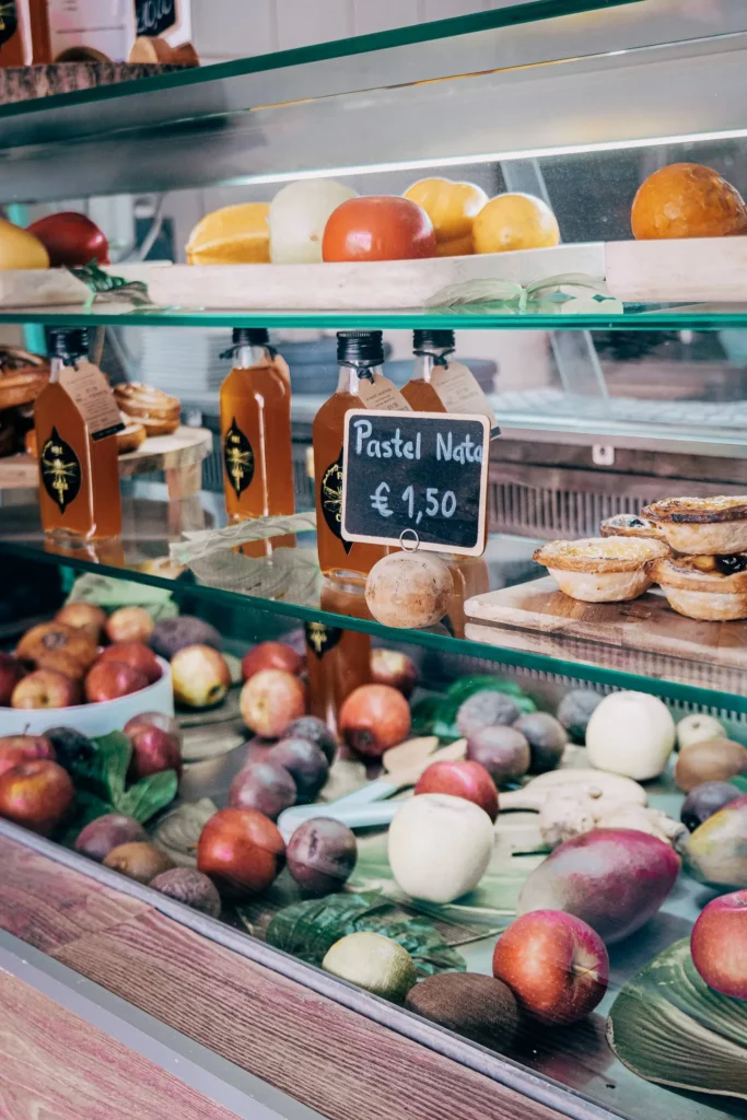 Restaurant showcase in Lagos displaying fresh fruits, bottles of juice, and pastéis de nata with a price tag. Typical atmosphere of a Portuguese pastry shop in the Algarve.