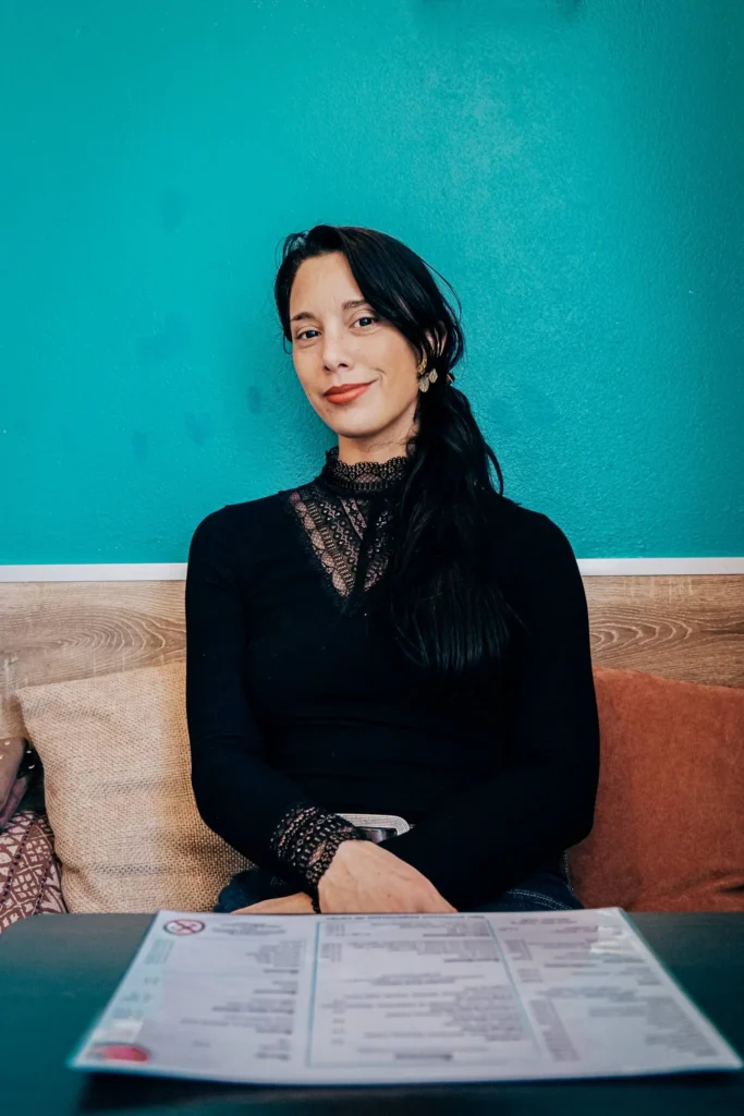 Caroline sitting at a table in the Goji restaurant in Lagos, Algarve, Portugal, with a menu in front of her and a turquoise wall in the background.