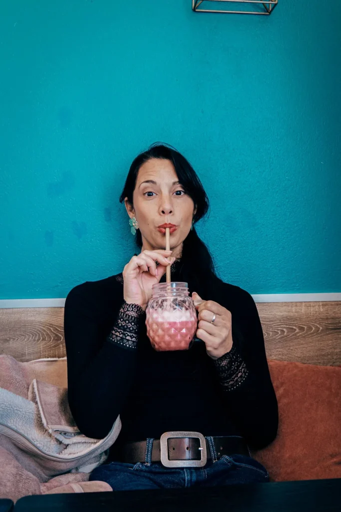 Caroline sitting in a restaurant in Lagos, Algarve, enjoying a pink drink in a patterned mug, in front of a turquoise wall.