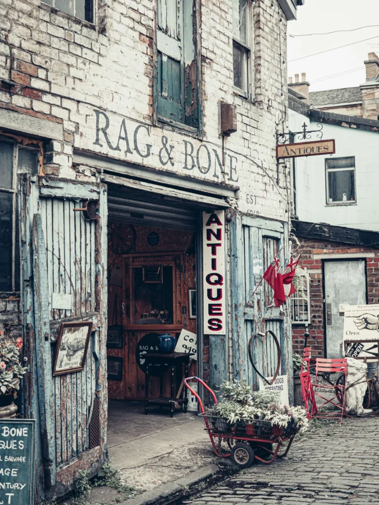Antique shop of The Hidden Lane, in Glasgow, a cart loaded with plants in front of the entrance and antique furniture visible inside. The antique dealers are part of what can be found in this artists' courtyard.