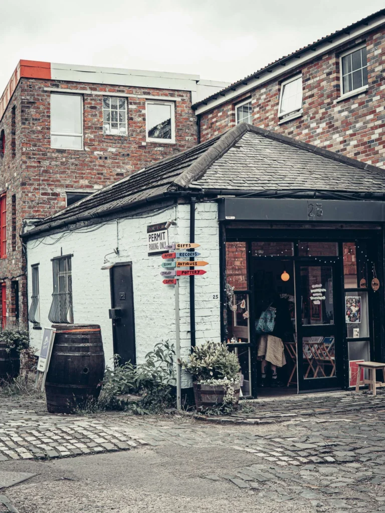 Caroline and Xavier in front of the door of an atelier at The Hidden Lane, in Glasgow, with a brick facade and potted plants on either side of the entrance.