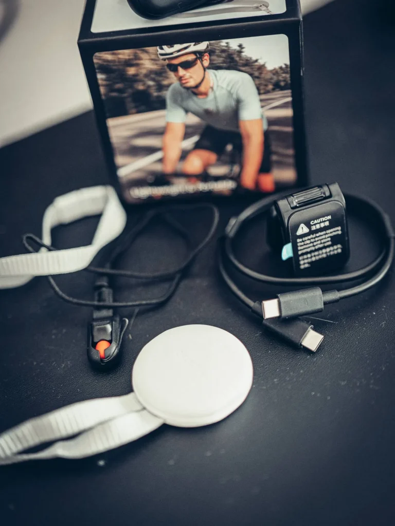 Close-up of the Insta360 GO Ultra accessories: the clip with its orange release button, the round magnetic mount and the double USB-C cable.