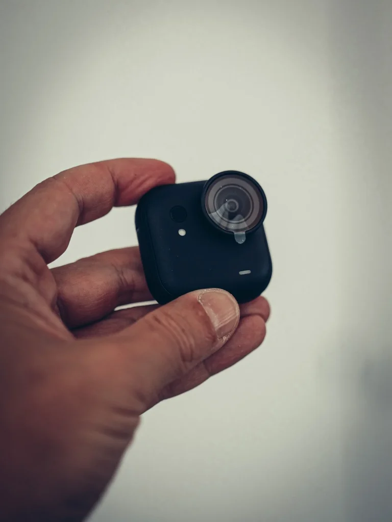 The Insta360 GO Ultra camera module held in hand, front face with the lens and the microphone, on a light background.