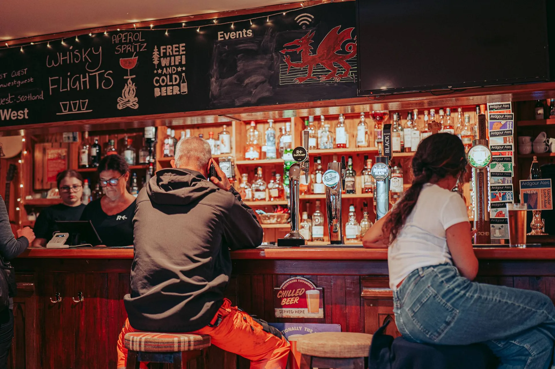 The bar at Roam West in Inchree, Onich, between Glencoe and Fort William, drinkers along the counter and a wall of bottles behind.
