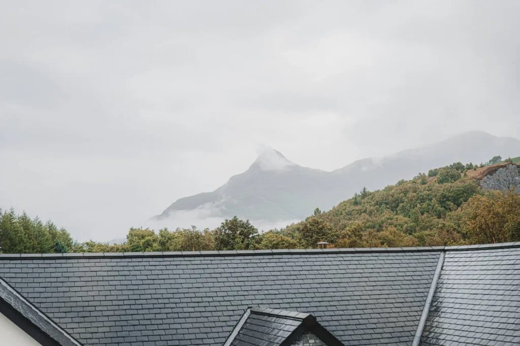 Slate roof of a house with a view of the misty mountains and the vegetation of the Highlands in Scotland, under a gray sky.