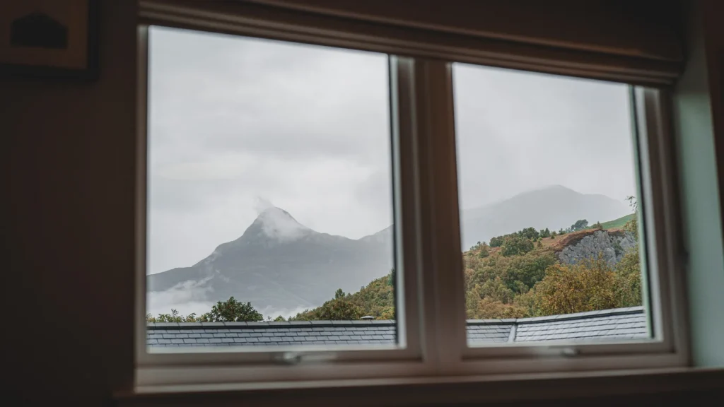 View of the Scottish Highlands mountains through a window, with a slate roof in the foreground and a cloudy atmosphere.