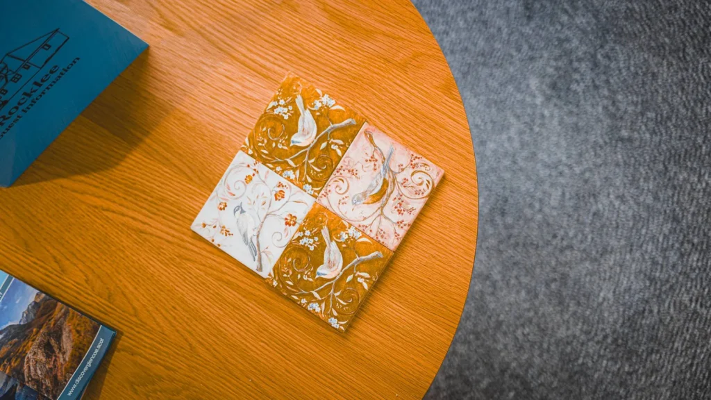 Ceramic coasters decorated with birds placed on a wooden table, with Rocklee Bnb brochures visible in the corner. Indoor atmosphere in Glencoe in the Scottish Highlands.