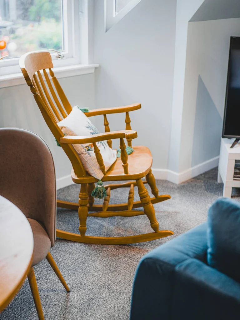 Wooden rocking chair with decorative cushion in a bright sitting room at Rocklee Bnb in the Scottish Highlands in August 2026.