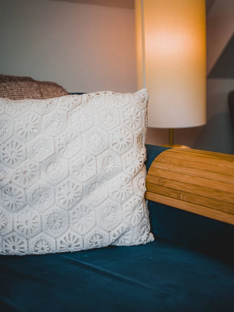 White knitted cushion on a blue sofa with a lit lamp in the background, warm indoor atmosphere in a Scottish Highlands accommodation.