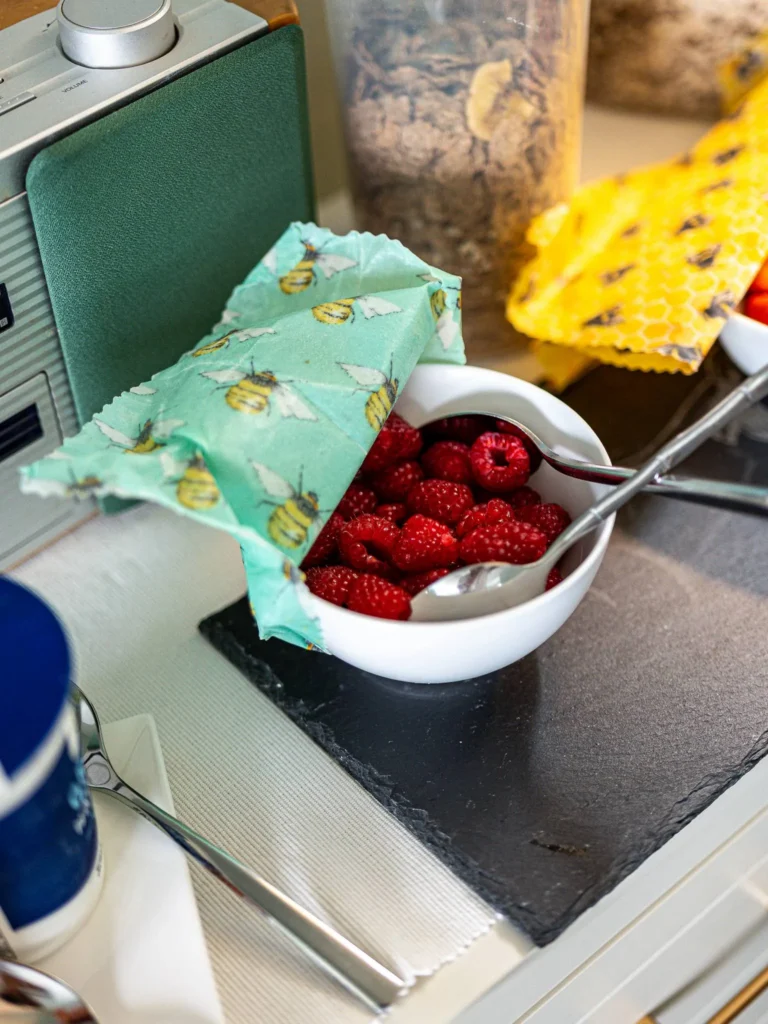 Bowl of fresh raspberries placed on a slate, with a fabric cover printed with bees, next to a vintage radio and a jar of cereal, in a breakfast setting at Rocklee Bnb in the Scottish Highlands.