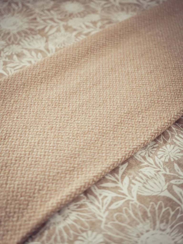 Close-up of a beige wool blanket laid on a floral patterned duvet cover, warm atmosphere typical of accommodation in the Scottish Highlands.