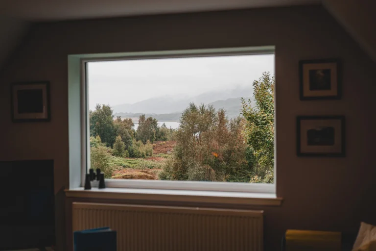 View from inside the house over a wooded, misty Highland landscape, with mountains behind and a radiator under the window.