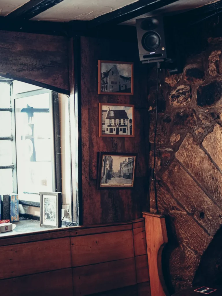 Wood and stone corner of the Settle Inn, in Stirling, with old photos on the wall and a speaker, in the dim light of the pub.
