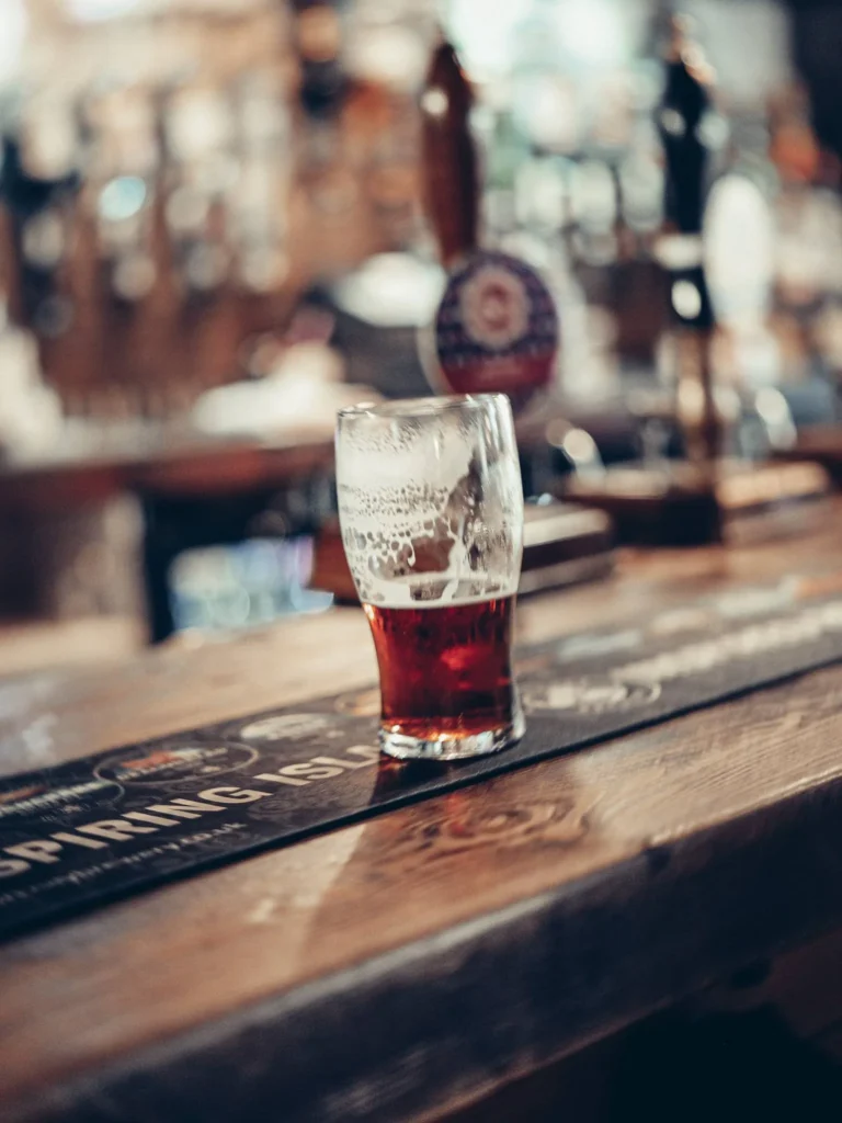 A half of amber beer on the wooden counter of the Settle Inn, in Stirling, with the beer taps in the background.