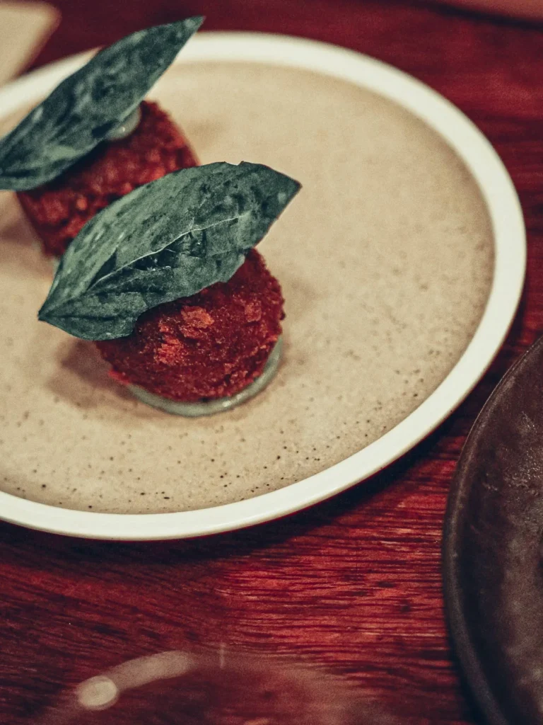 Two breaded bites presented on a stand and topped with a large leaf, served at Stravaigin in Glasgow on 14 August 2026. Dish not identified on the menu recorded that day.