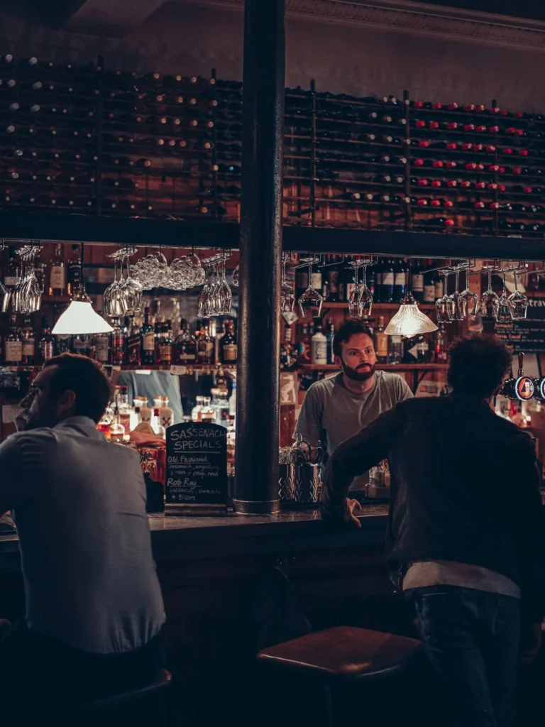 The bar at Stravaigin, Glasgow: wooden counter, heavy central pillar and lined-up bottles, two customers chatting to the barman.