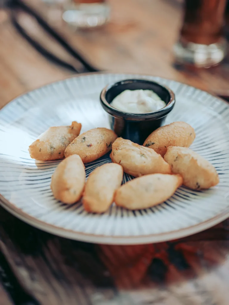Plate of pasteis de bacalhau served with a white sauce on a wooden table at The Garden Bar and Grill in Lagos.