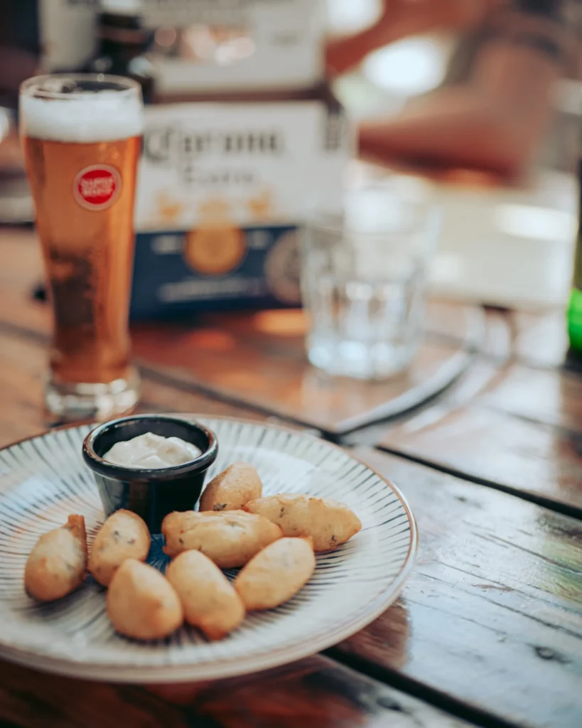 Codfish cakes with their white sauce accompanied by a Super Bock beer, on a wooden table at The Garden Bar and Grill in Lagos.
