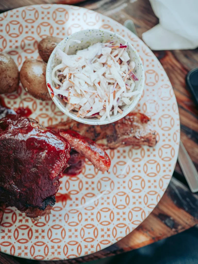 Mixed meat from The Garden Bar and Grill in Lagos viewed from above: half-ribs covered in barbecue sauce, sausage, grilled bacon, potatoes, and coleslaw.