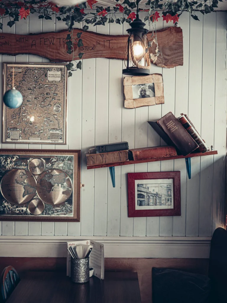 Corner of the room decorated at The Geographer in Fort William, featuring old maps, books, a hanging lantern, and decorative elements on a light wood wall.