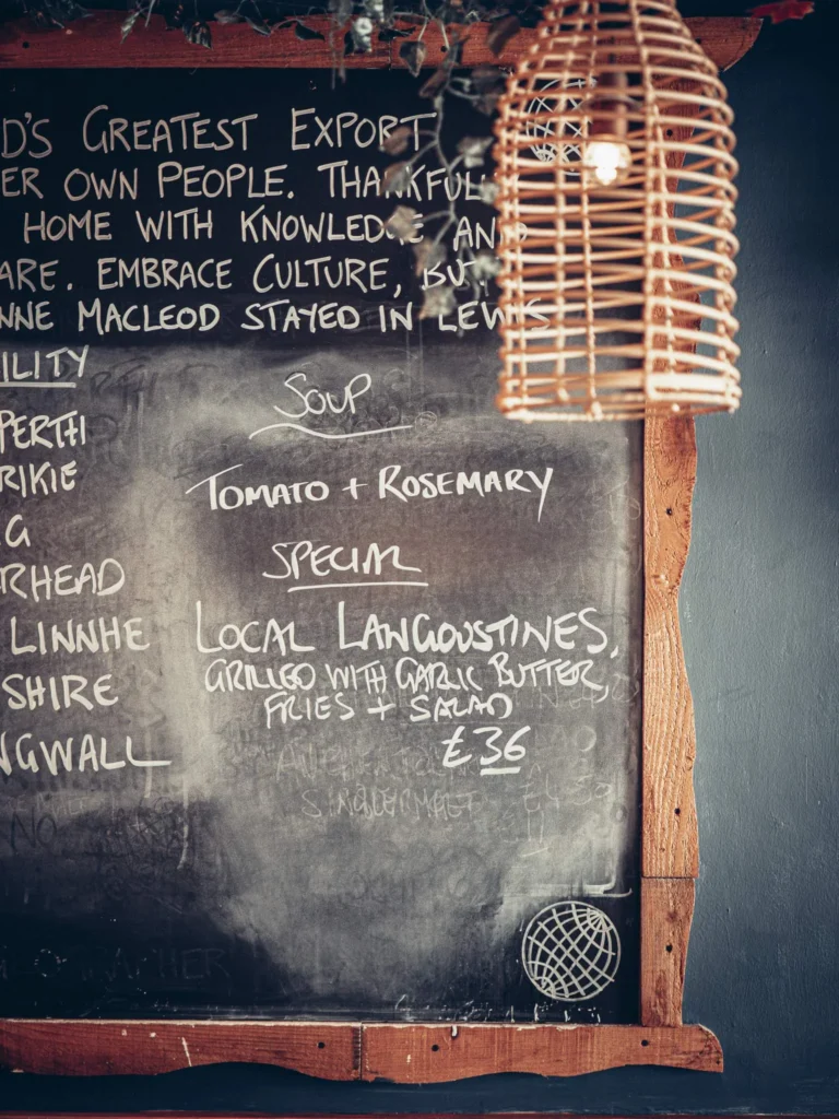 Slate of the day at The Geographer in Fort William, announcing a rosemary tomato soup and locally grilled langoustines, under a wicker pendant.