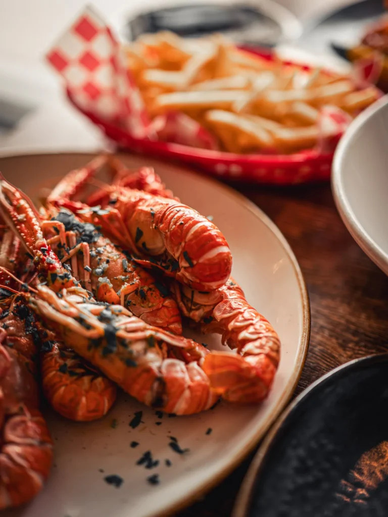 Grilled local langoustines seasoned, served on a wooden table with a basket of fries, at The Geographer in Fort William.