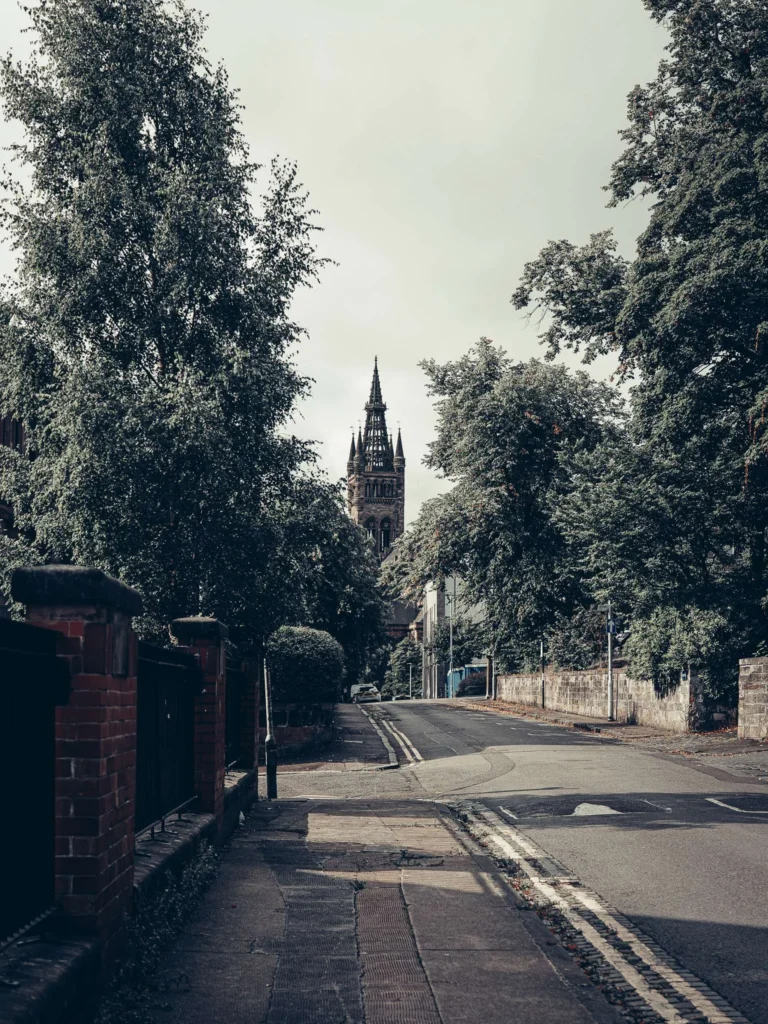 Quiet, tree-lined street in the West End of Glasgow, with the neo-Gothic tower of the Main Building of the university in the background.