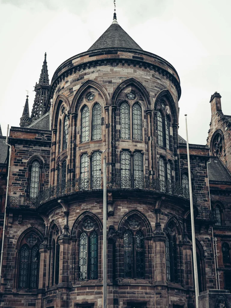 Stone facade of the University of Glasgow: large pointed arch windows and turret, in the neo-Gothic style of the campus.