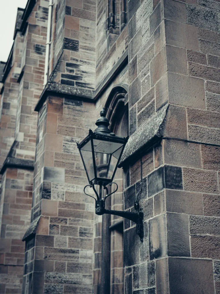 Old lantern fixed on a stone wall of the University of Glasgow.