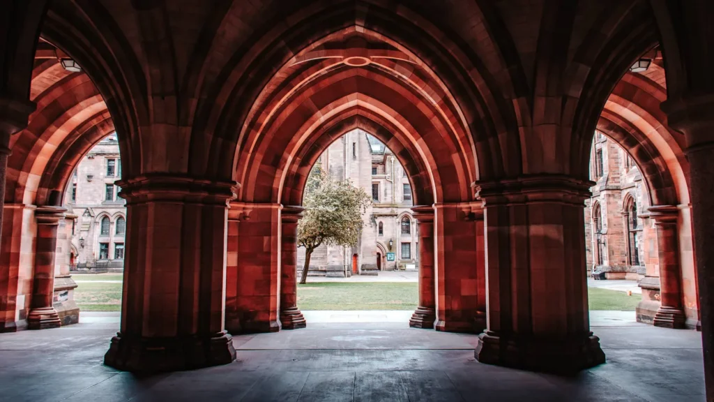 The Gothic arches of a cloister at the University of Glasgow, looking onto a quadrangle with a tree at its centre.