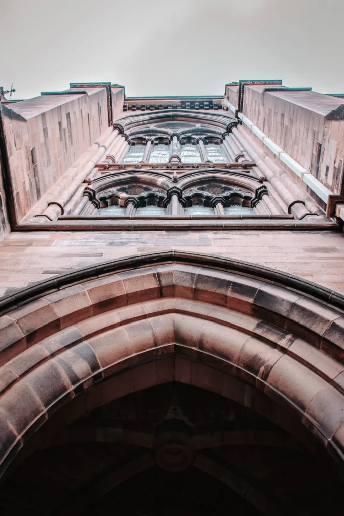 Facade of a stone neogothic building of the University of Glasgow, viewed from below under an imposing arch.