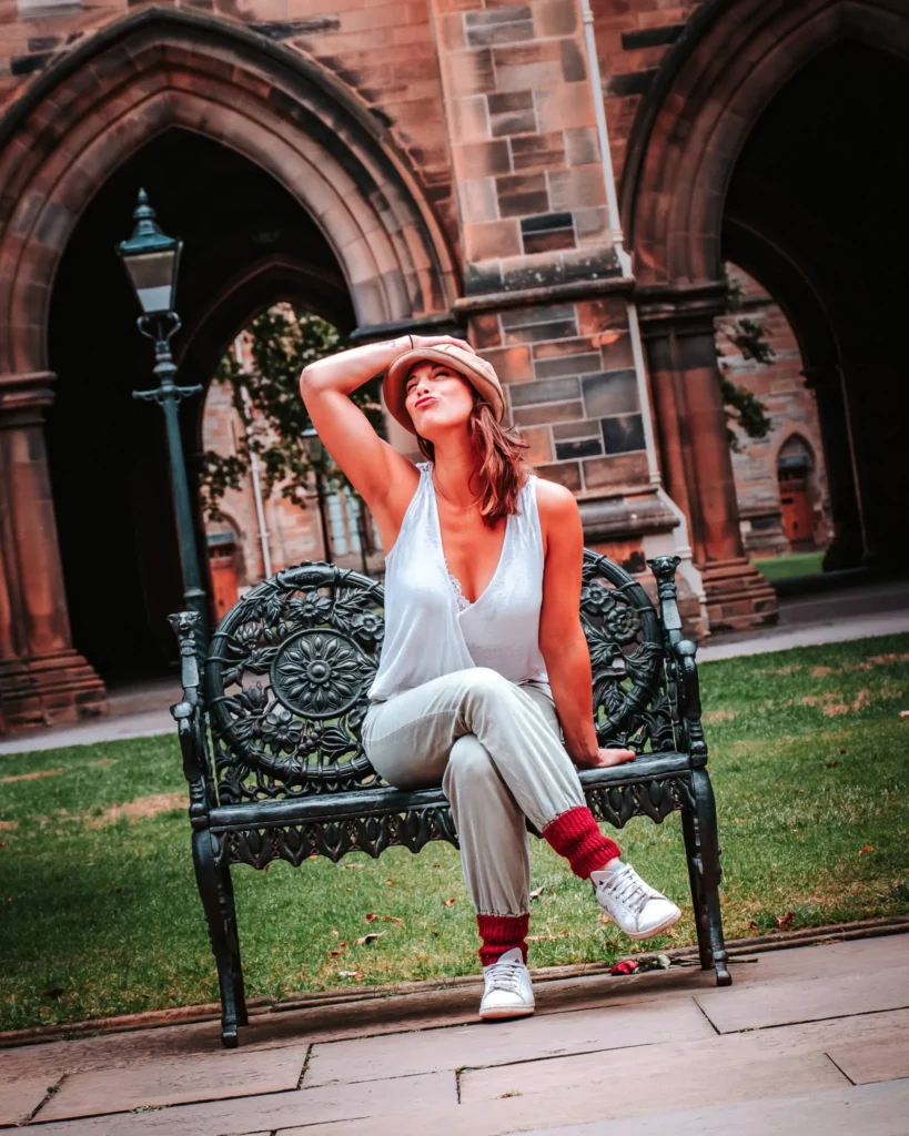 Caroline sitting on a wrought iron bench in a Gothic courtyard of the University of Glasgow, Scotland, in summer.