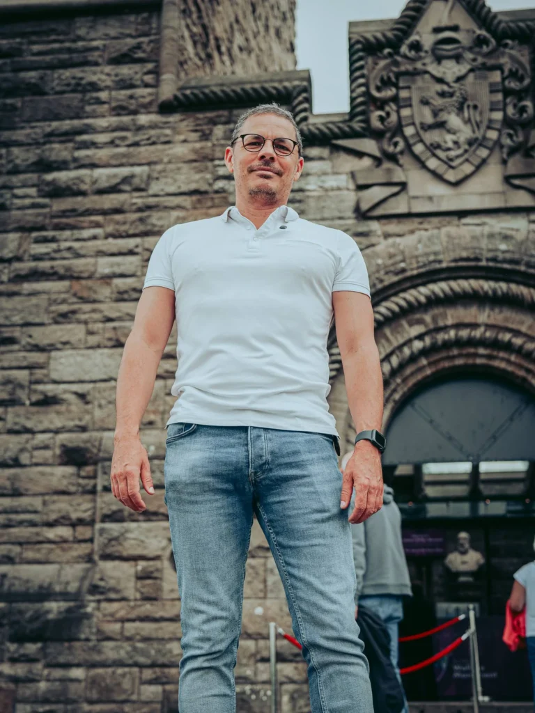 Xavier in front of the entrance to the Wallace Monument in Stirling, Scotland, on 17 August 2026, with the stone facade and the coat of arms behind him.