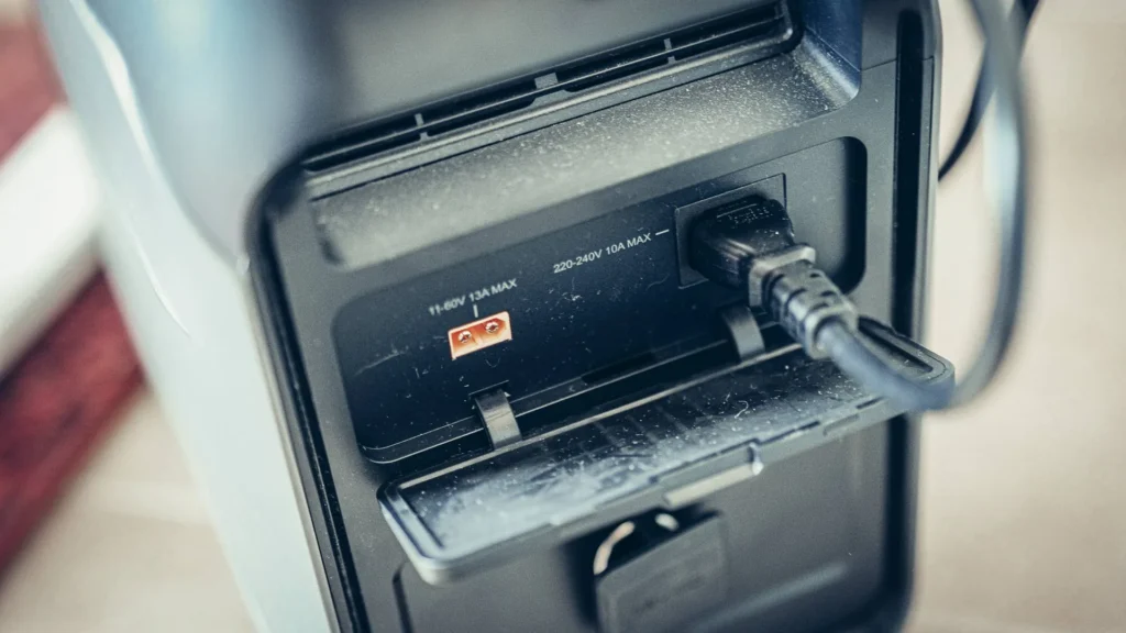 Close-up of the ALLPOWERS P1800 showing two input ports: an 11-60 V 13 A MAX input and a 220-240 V 10 A MAX AC input, with a plugged cable.