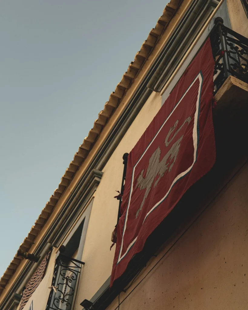 Red medieval banner hanging from a balcony on the facade of a building in Castro Marim, Algarve, under a clear sky in May 2023.