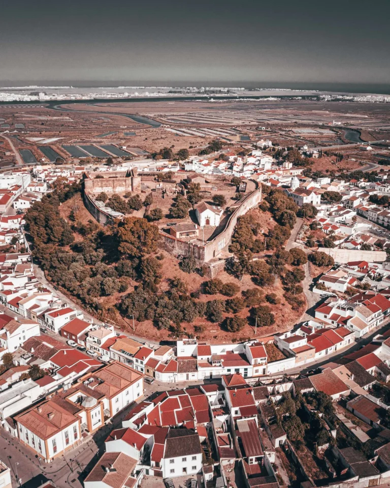 Aerial view of the Castro Marim castle surrounded by traditional red-roofed houses, with the salt marshes of the Algarve in the background, taken in May 2024.