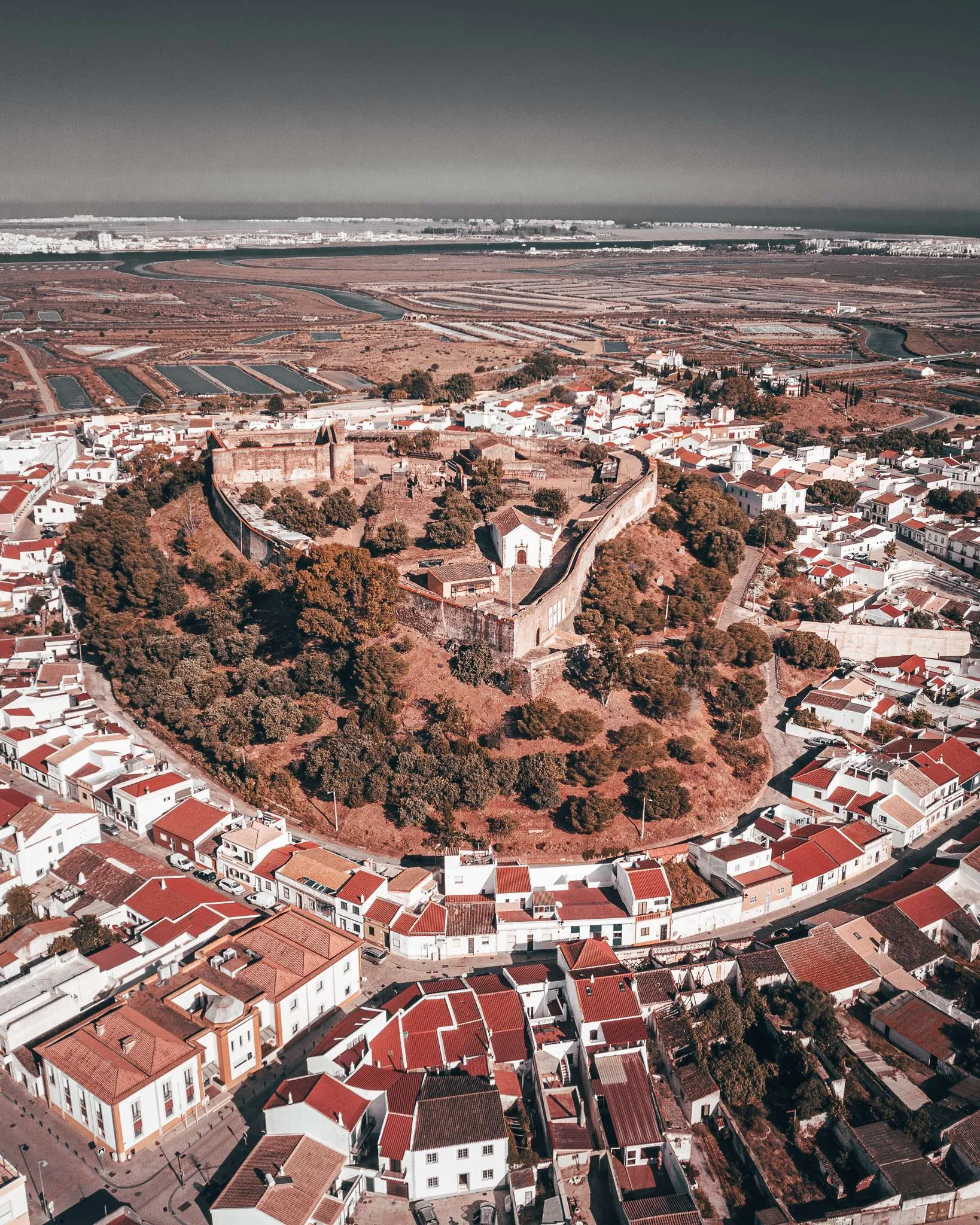 Aerial view of the Castro Marim castle surrounded by traditional red-roofed houses, with the salt marshes of the Algarve in the background, taken in May 2024.