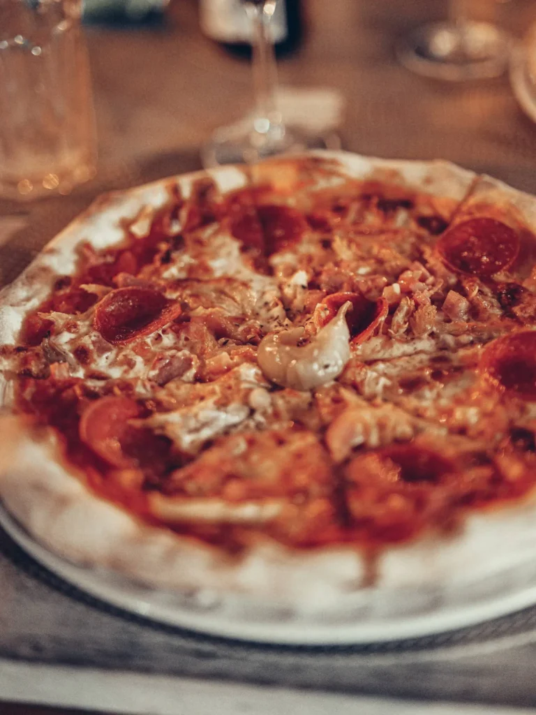 Pizza topped with cold cuts and cheese on a restaurant table, warm atmosphere typical of a pizzeria in Tavira, Algarve.