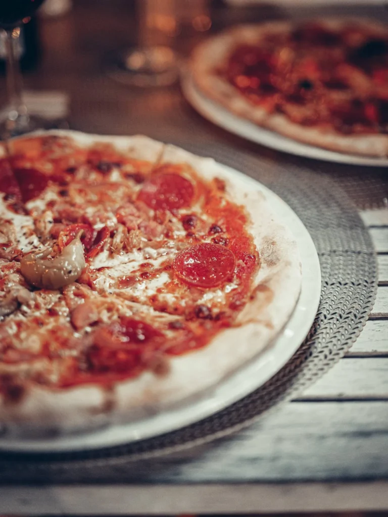Two topped pizzas are placed on a restaurant table, warm indoor atmosphere in Tavira, Algarve.